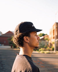 Cassowary Drive Short Brim Logo Hat — side profile, golden hour outdoor